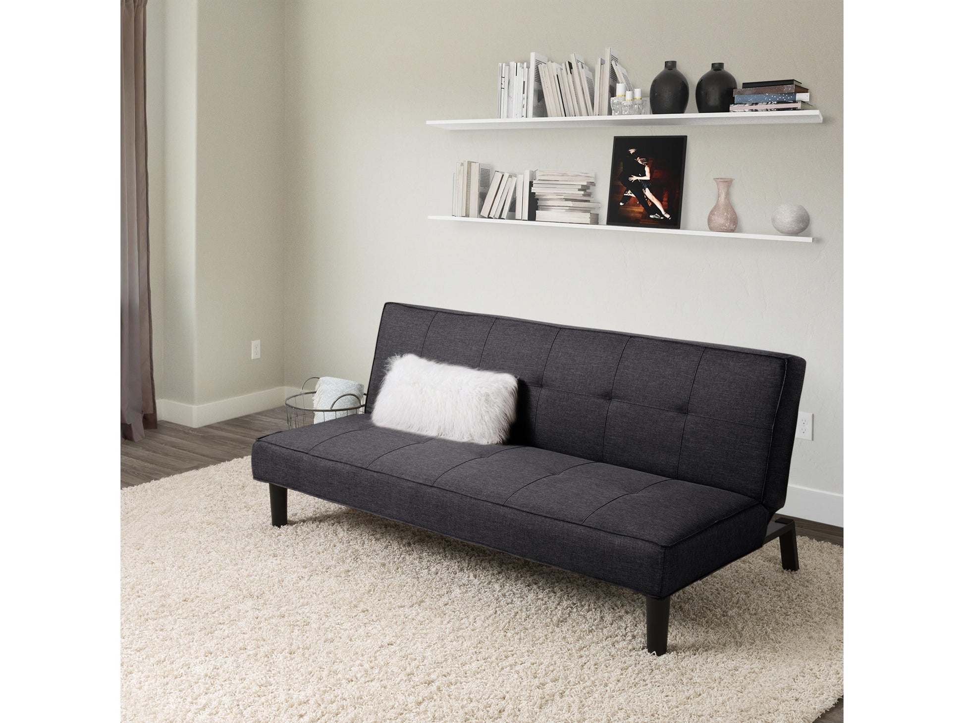 Dark grey futon sofa bed with tufted cushions, wooden legs, and a sleek, modern design.