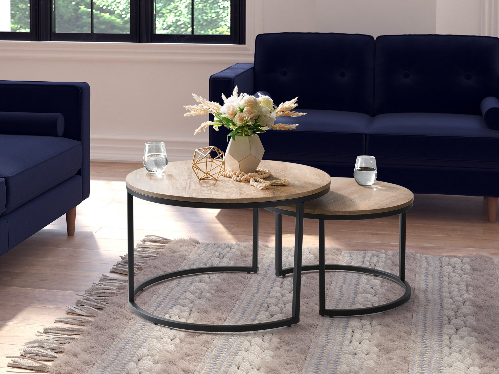 Light wood round nesting coffee tables with black metal legs and minimalist design.