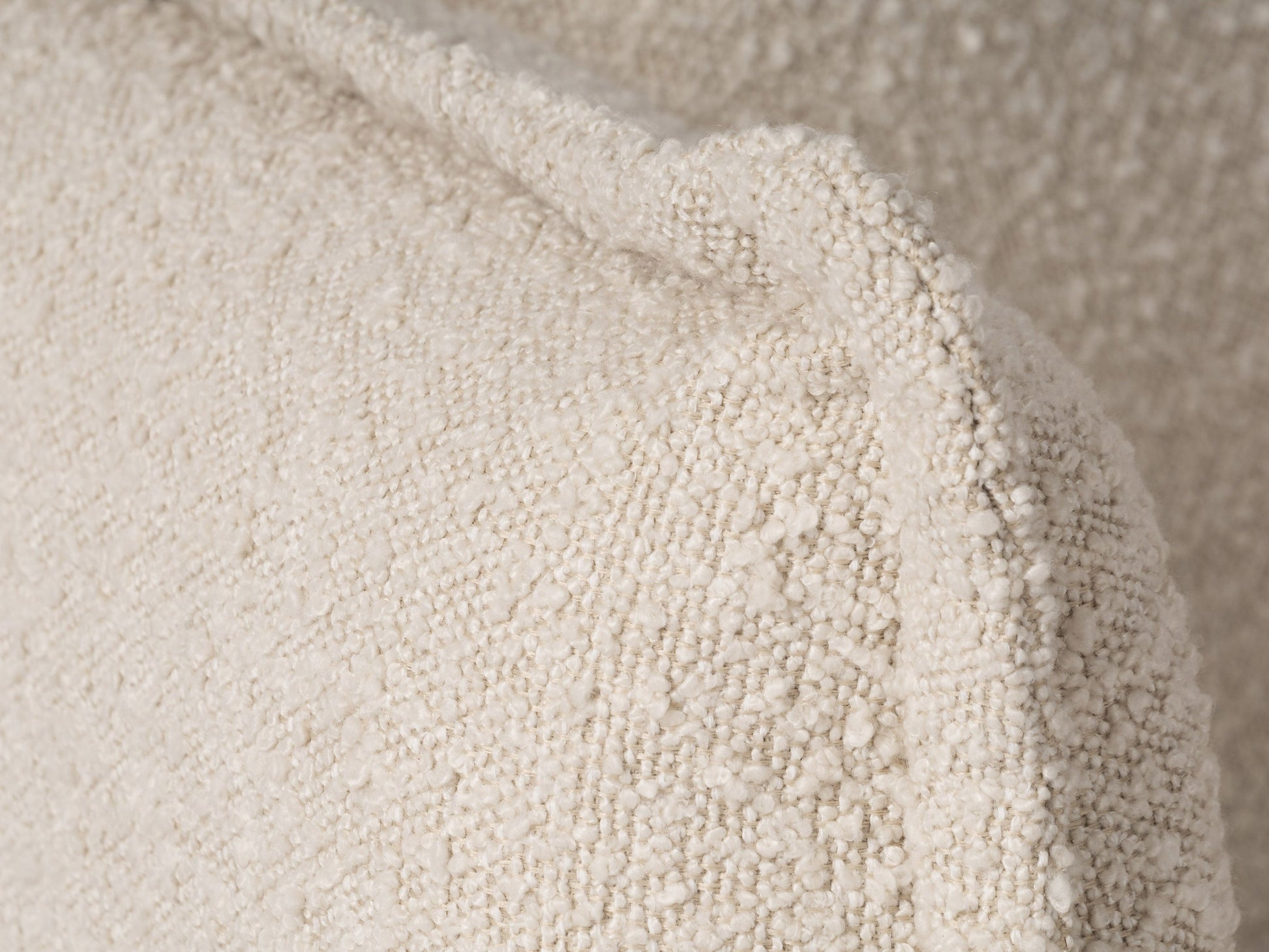 Boucle sofa with cream upholstery, curved silhouette, and wooden legs for modern living rooms.