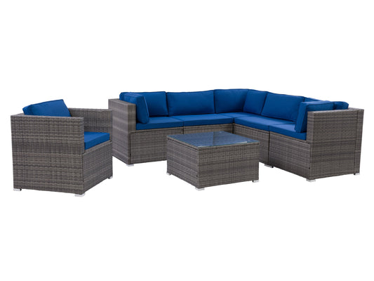 Modern patio sectional in gray wicker with beige cushions, featuring a square glass-top coffee table and decorative throw pillows, set on a wooden deck with green plants in the background.