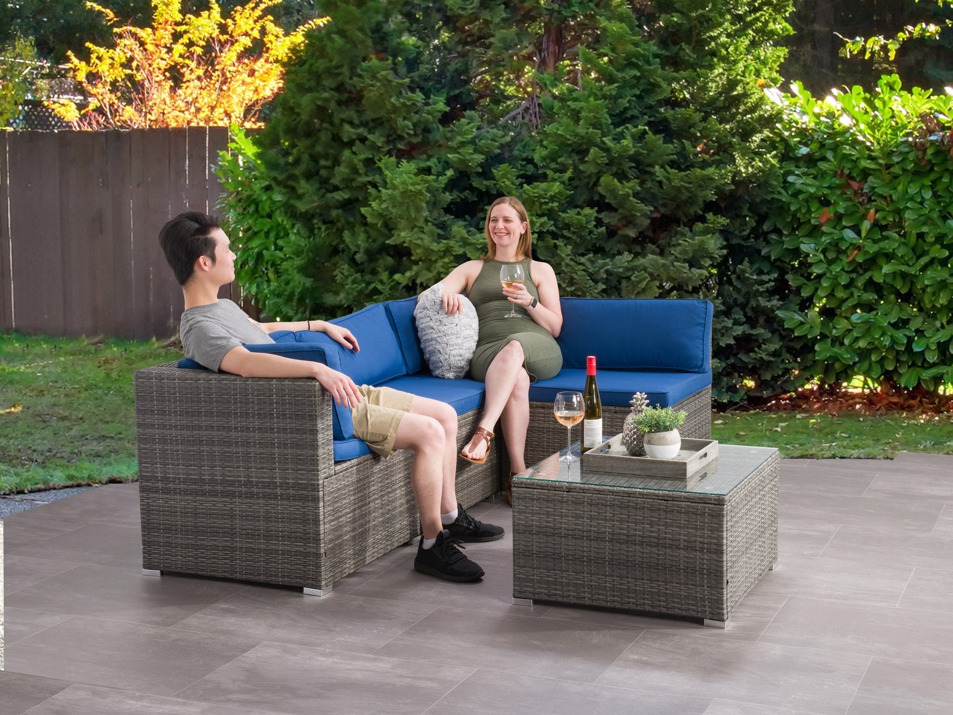 Gray outdoor patio sectional with plush cushions, modern design, and durable wicker frame. Set includes a matching coffee table with a glass top, perfect for garden or backyard lounging.
