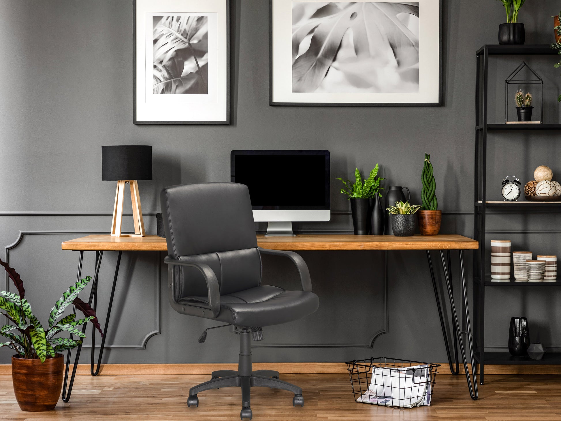 Elegant black leather office chair with adjustable armrests, high back support, and chrome base on casters, placed in a modern office setting with a wooden desk and plant in the background.